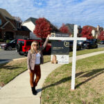 Kelly Ettrich, professional real estate agent in Loudoun County, smiling next to a 'For Sale' sign outside a beautiful property.