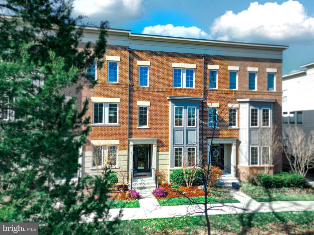 
Modern three-story townhouse at 22914 Bollinger Terrace, Ashburn, VA 20148, showcasing a stylish brick facade with bay windows and elegant entryway. The property is framed by mature trees and well-maintained landscaping, reflecting a blend of urban design with natural surroundings