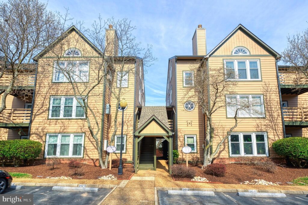 
Charming multi-unit residential building at 241 Loudoun St SW Unit F, Leesburg, VA 20175, featuring a beige wooden siding exterior with contrasting green trim and shutters. The central entrance is accentuated by a peaked roofline and flanked by symmetrically placed windows with round decorative elements above