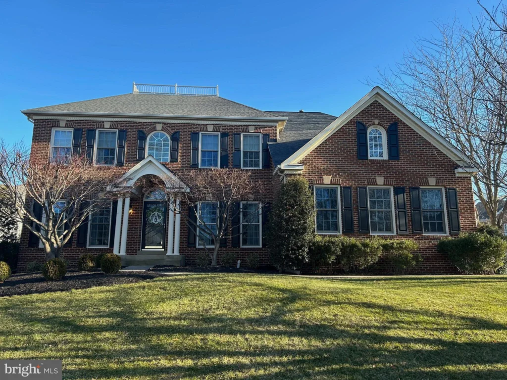 
Elegant brick front colonial home at 42650 FAIRWEATHER, BROADLANDS, VA 20148, featuring a symmetrical design with a central arched entryway, flanked by sash windows with contrasting shutters. Dormer windows adorn the roof, adding character to the facade amidst leafless trees and a lush green lawn