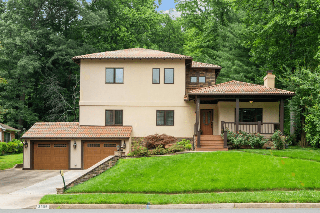 Beautiful two-story home for sale in Falls Church with a beige exterior, brown trim, and a well-maintained lawn, surrounded by lush greenery.