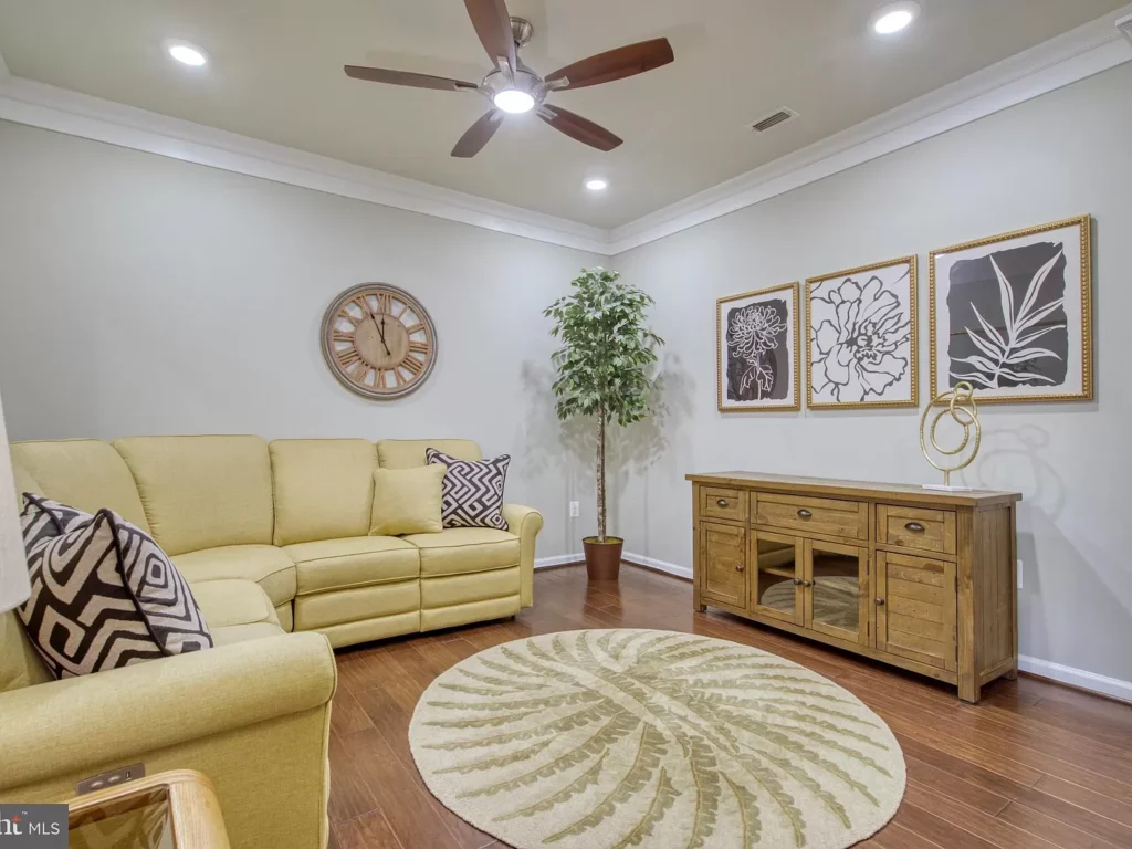 Beautifully furnished living room with yellow sofa, wooden cabinet, round rug, and decorative artwork, located in a rental unit at Potomac Green, Ashburn, VA.