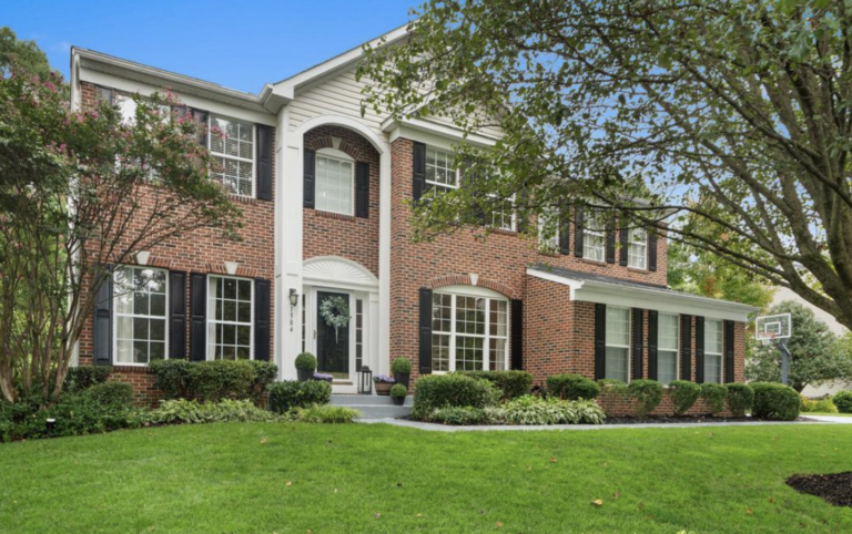 Colonial-style brick home with black shutters and manicured lawn